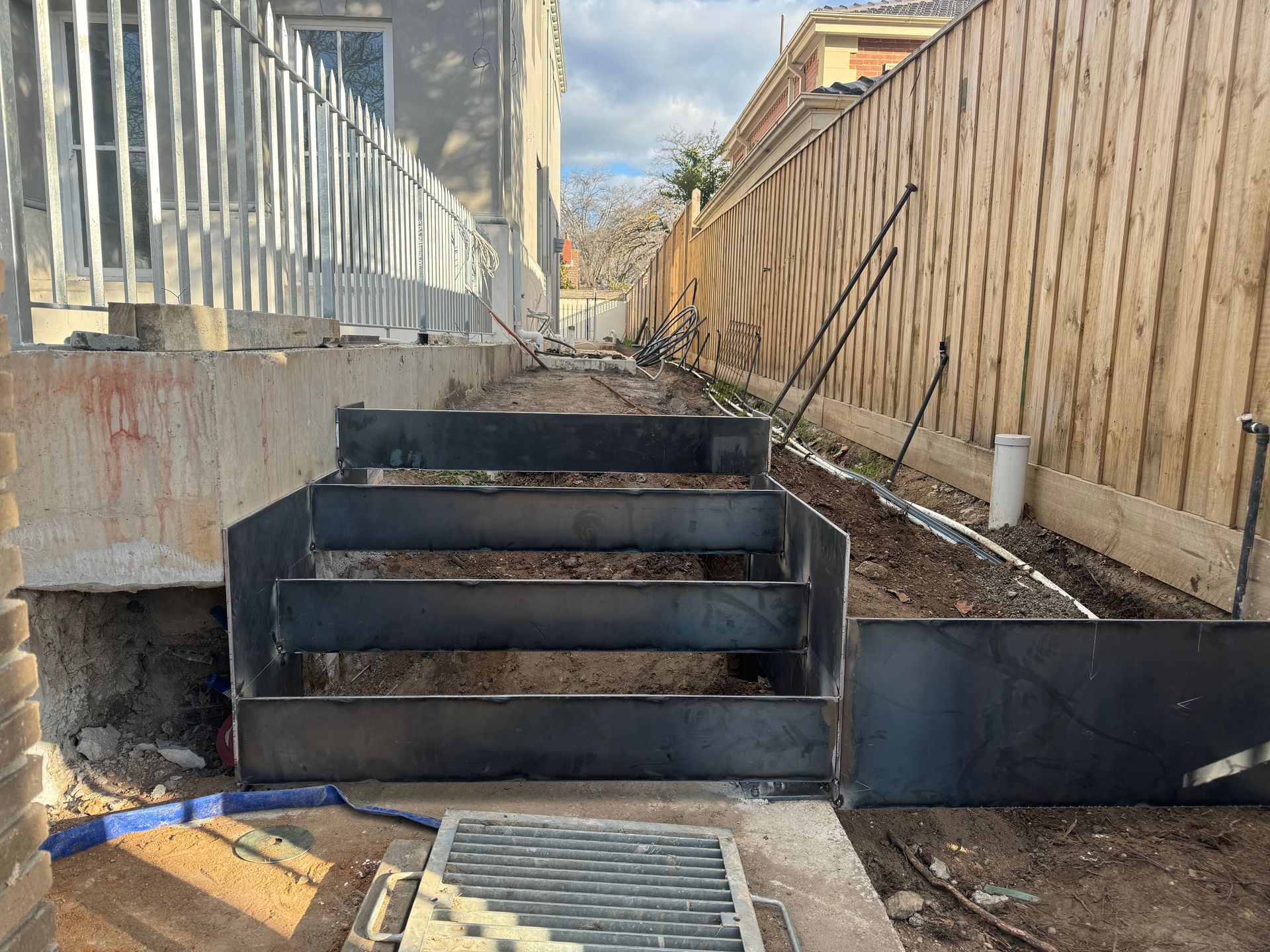 Outdoor concrete stairway under construction beside a wooden fence, with black steps and debris nearby