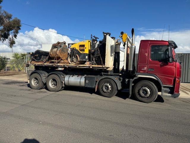 Red truck transporting construction equipment on a flatbed, parked on asphalt.