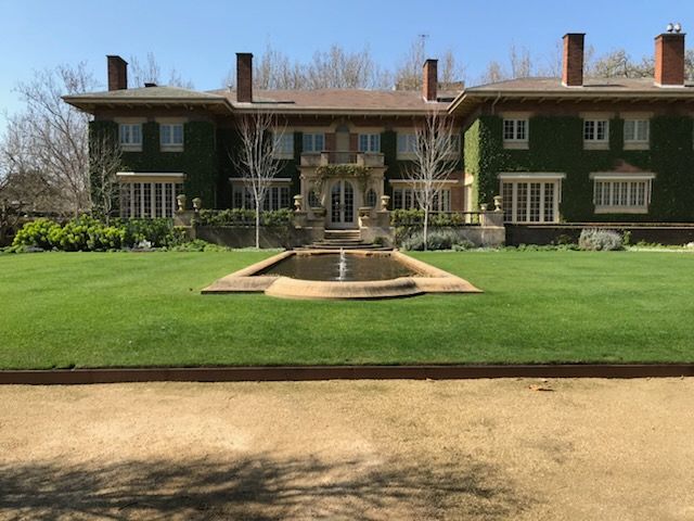Large ivy-covered mansion with a central fountain and wide green lawn under a clear blue sky