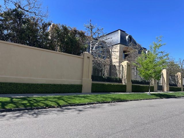 Tall beige wall and stone building beside a quiet street under a clear blue sky
