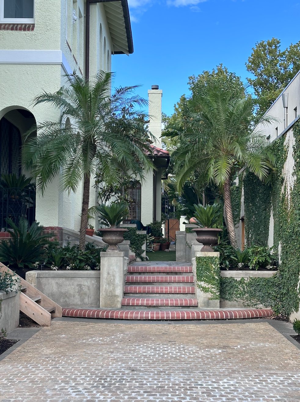 Mediterranean-style courtyard with steps, potted palms, and a cobblestone driveway