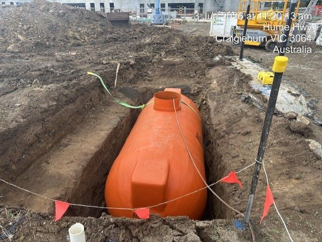 Orange underground storage tank in a construction trench, with warning flags and mud around it