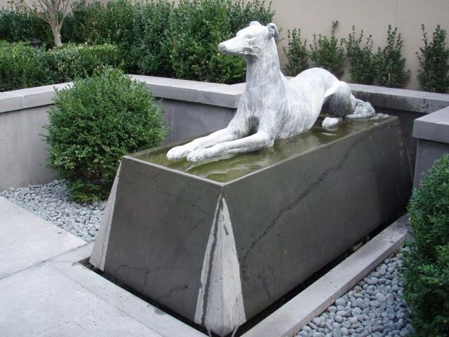 A statue of a dog laying on a rock in a garden