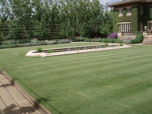 A large lawn with a fountain in the middle and a house in the background.