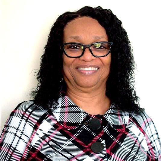 Woman wearing glasses and plaid jacket, smiling at the camera.