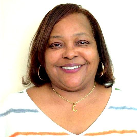 Woman with brown hair smiling, wearing a gold necklace, and a striped shirt against a white background.