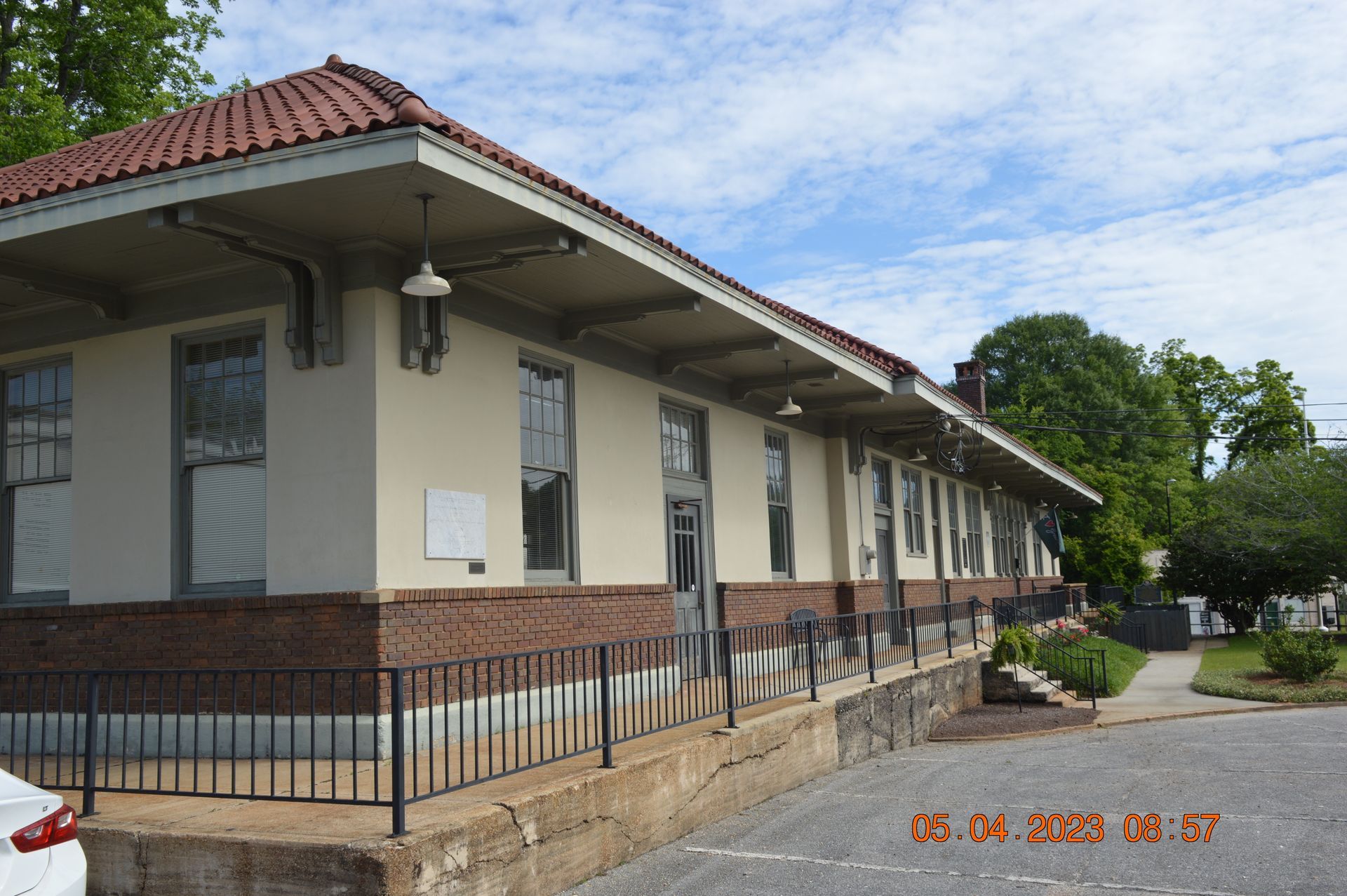 Low-angle view of a beige and brick building with a red-tiled roof, windows, and a metal railing.