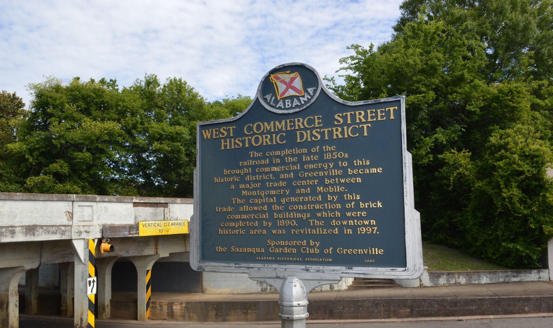 Historical marker for West Commerce Street Historic District, dark sign, bridge in background.