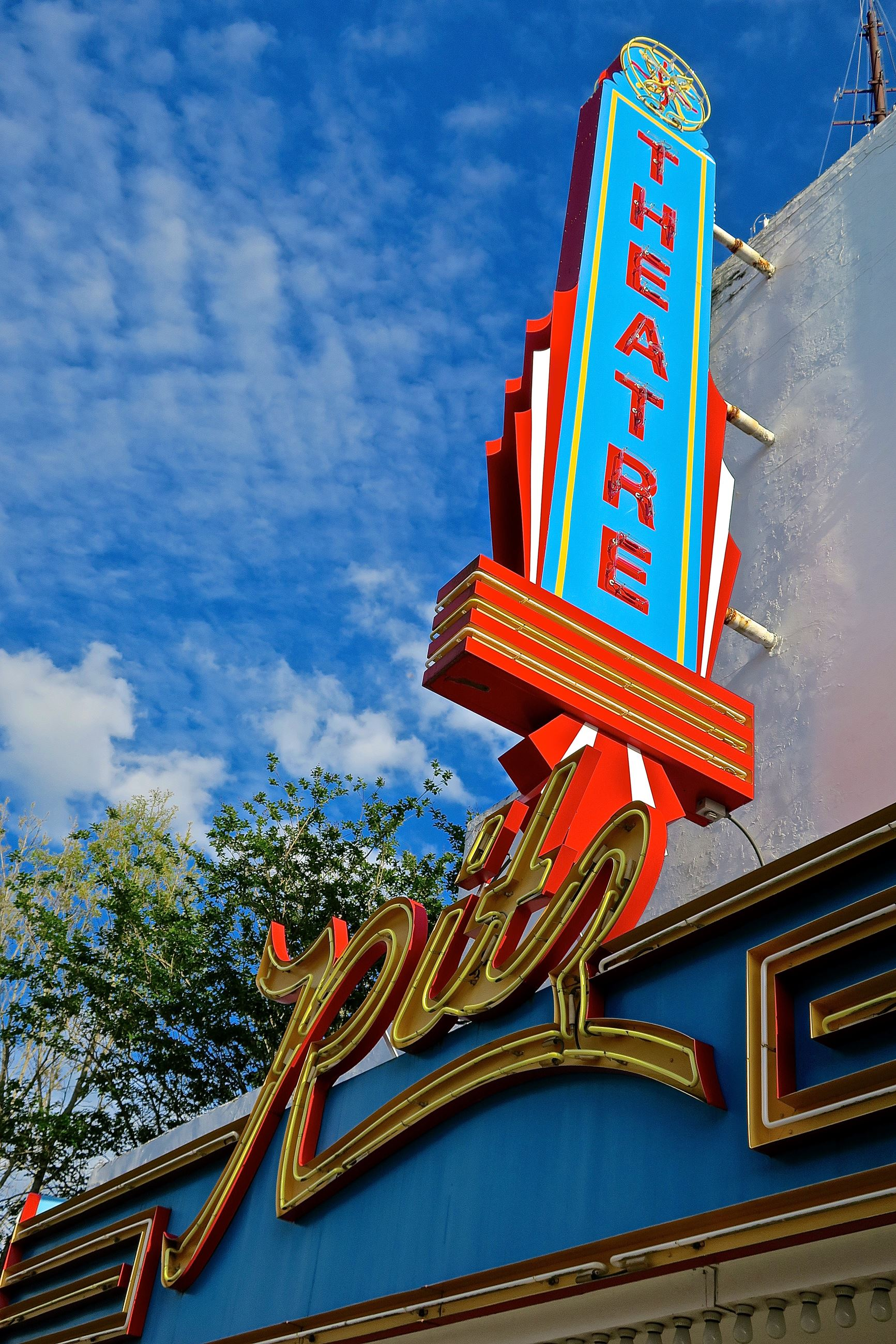 Retro theater sign in teal, red, and gold against a blue sky, reading 