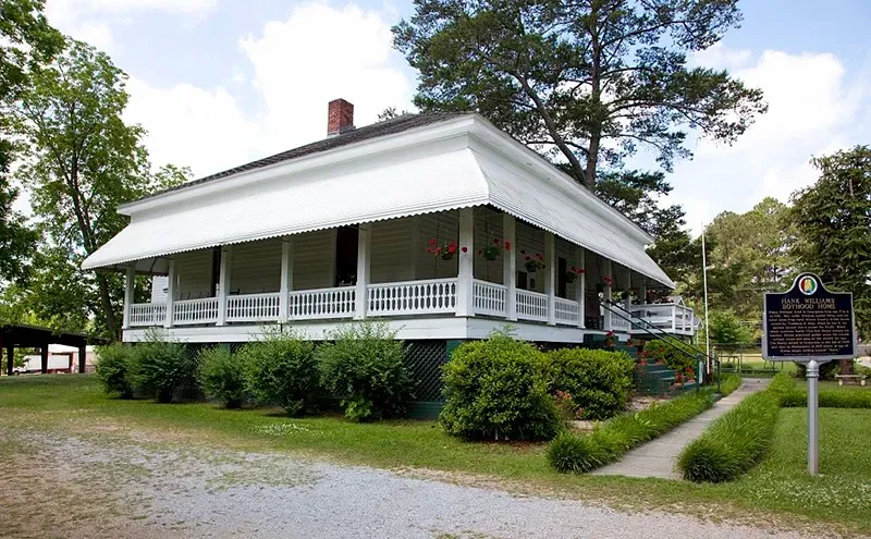 White historic home with wide porch and sign on the lawn.