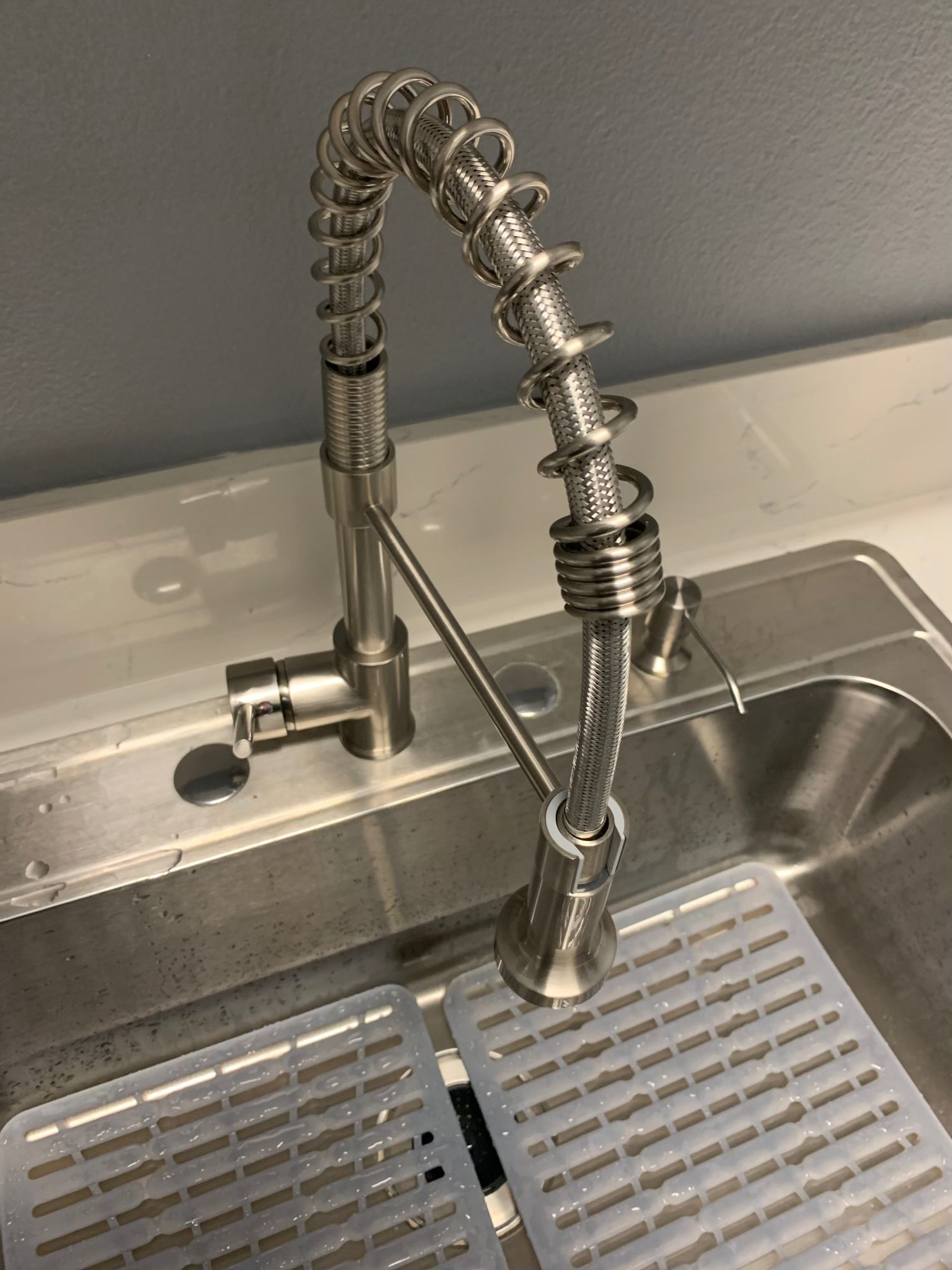A brushed nickel industrial-style pull-down kitchen faucet positioned over a stainless steel sink with sink mats.