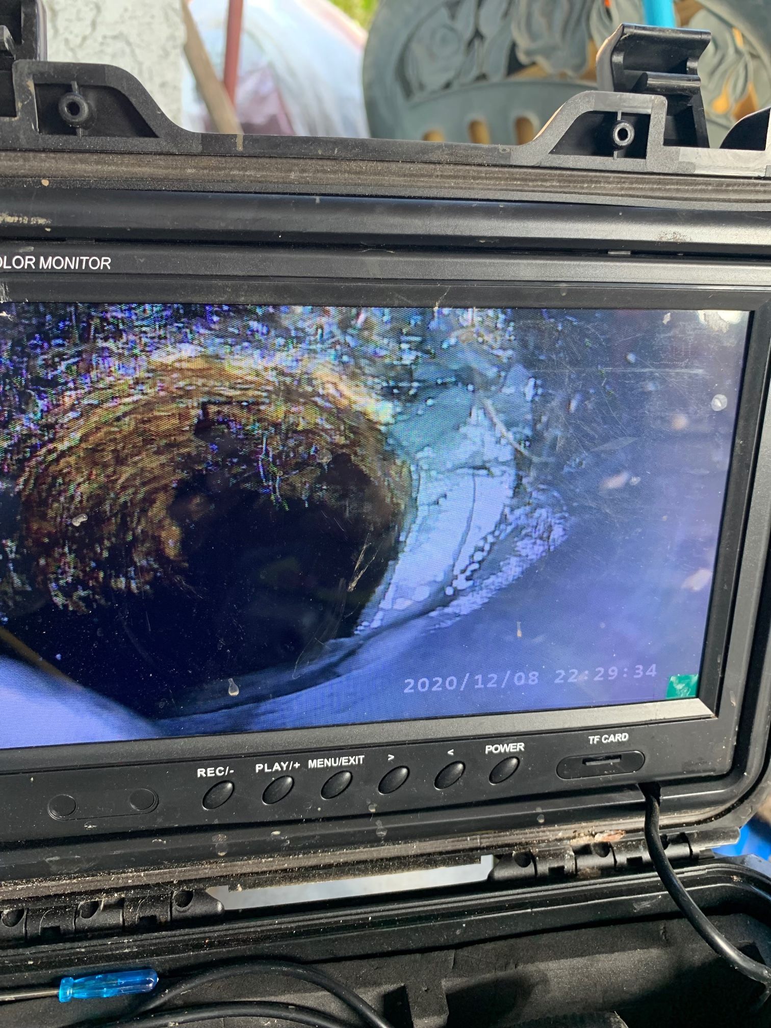 A sewer camera monitor displays an internal view of a pipe with significant buildup and obstruction.