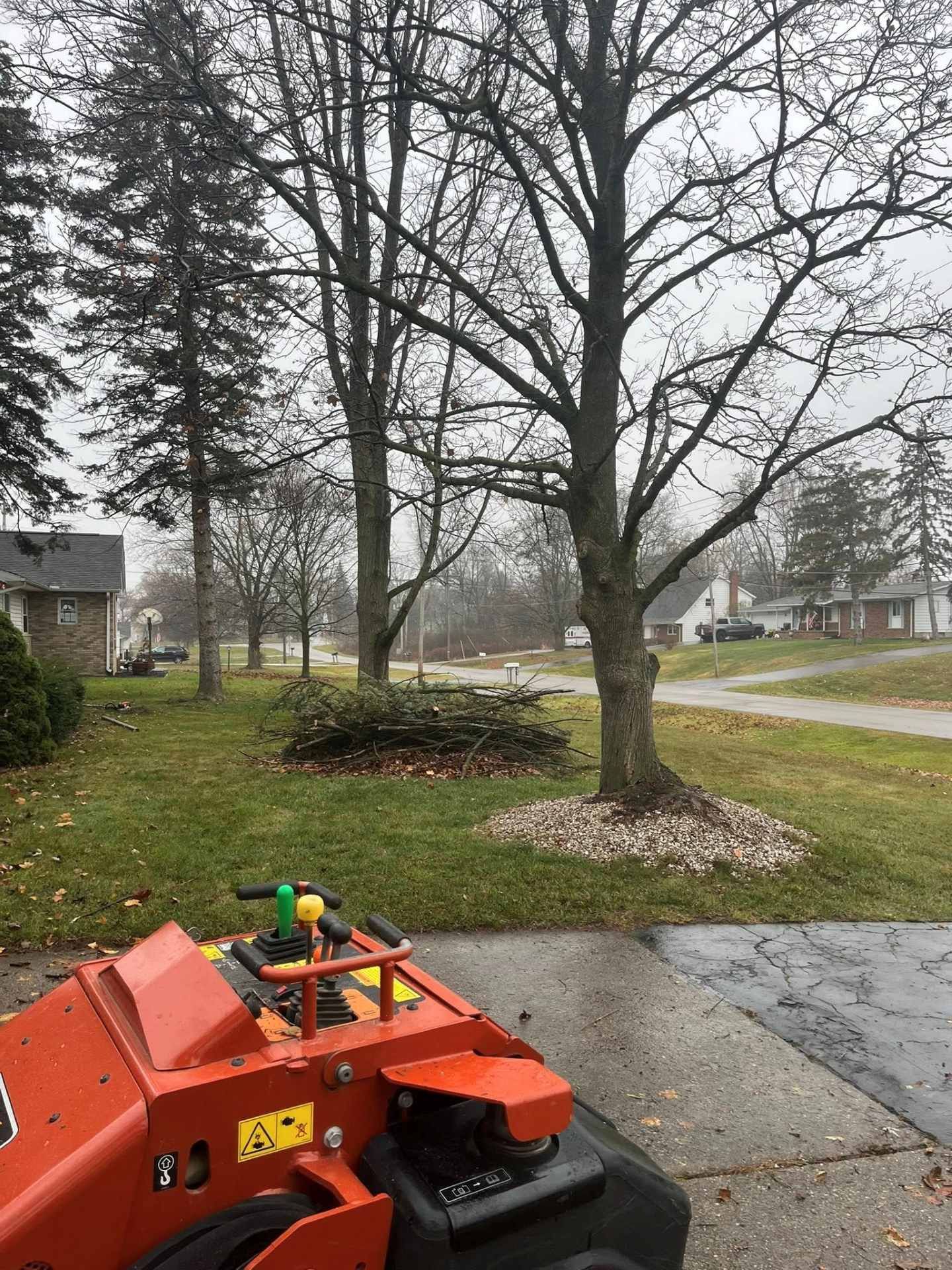 Orange lawn mower in driveway beside leafless tree and suburban yard