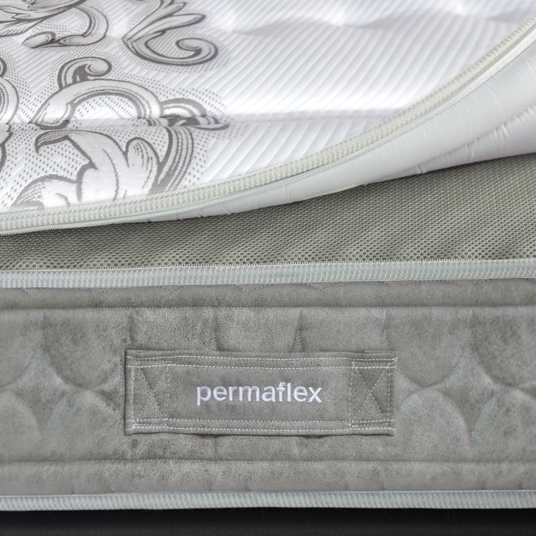 Primo piano di un materasso Permaflex che mostra uno strato superiore bianco con motivo decorativo e un pannello laterale grigio trapuntato con etichetta del logo.