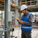Obrero con casco utilizando una tableta junto a un panel eléctrico en una obra de construcción.