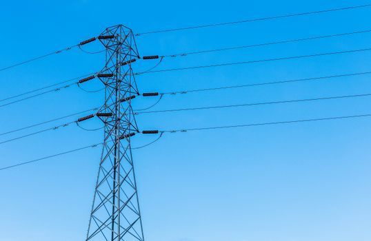 Torre de transmisión de alta tensión con líneas eléctricas contra un cielo azul despejado.