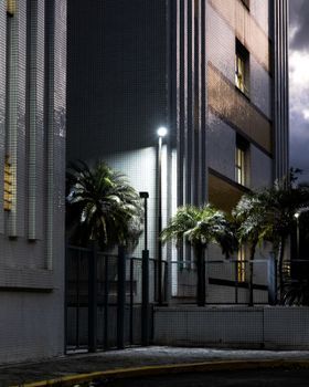 Vista nocturna de un moderno edificio de apartamentos con palmeras y luces exteriores brillantes.