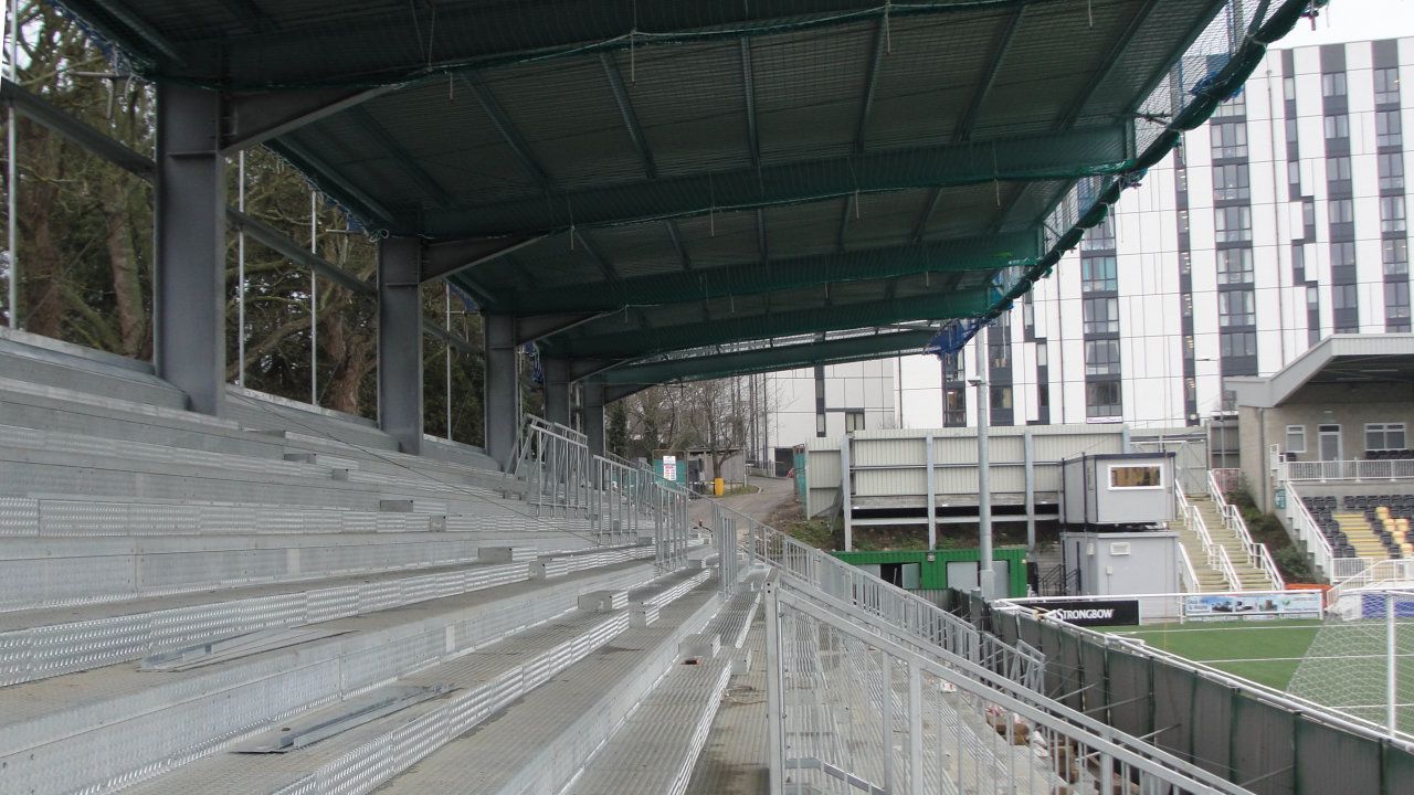 A stadium with a canopy over the bleachers and a building in the background.