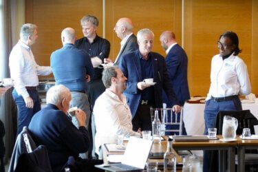 A group of men are sitting at tables in a room talking to each other.