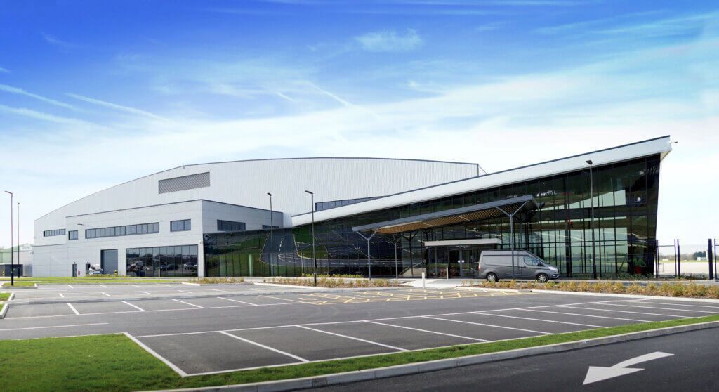 An artist 's impression of a large  Reidsteel aircraft hangar with a parking lot in front of it.