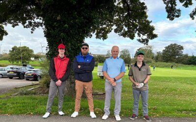 A group of men are standing under a tree on a golf course.