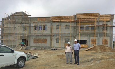 Two men are standing in front of a Reidsteel school building under construction.