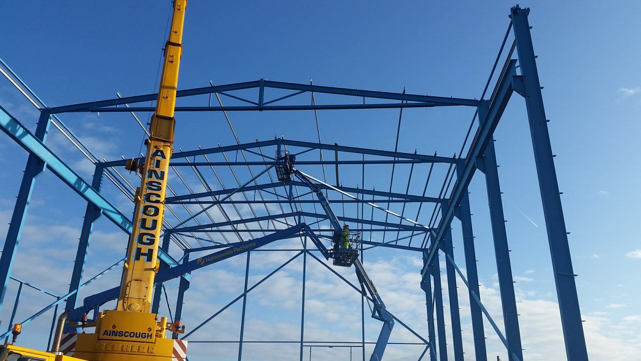 A yellow crane is working on a building under construction.