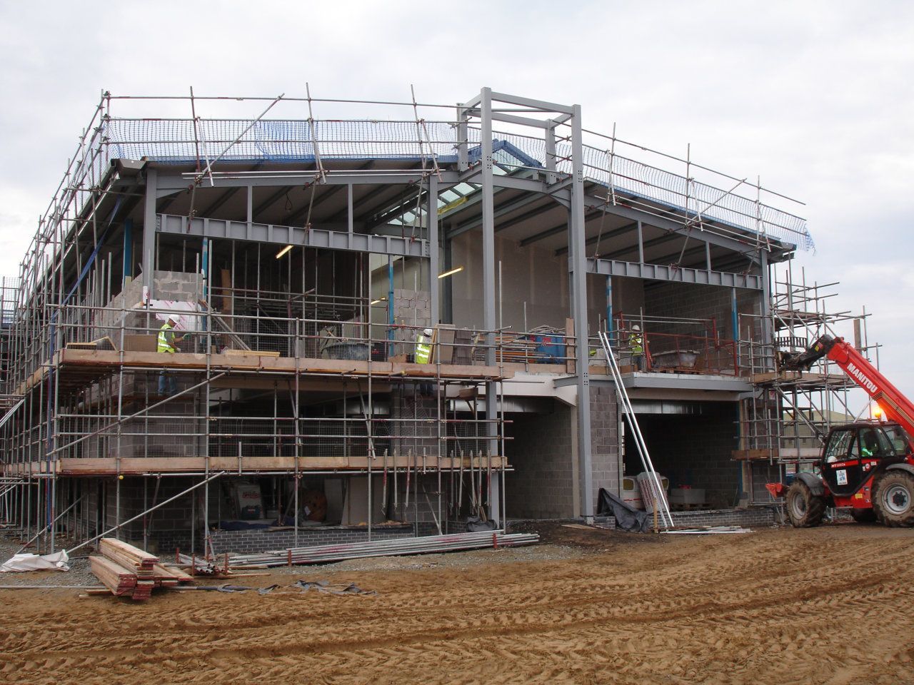 A large building is being built with scaffolding and a forklift.