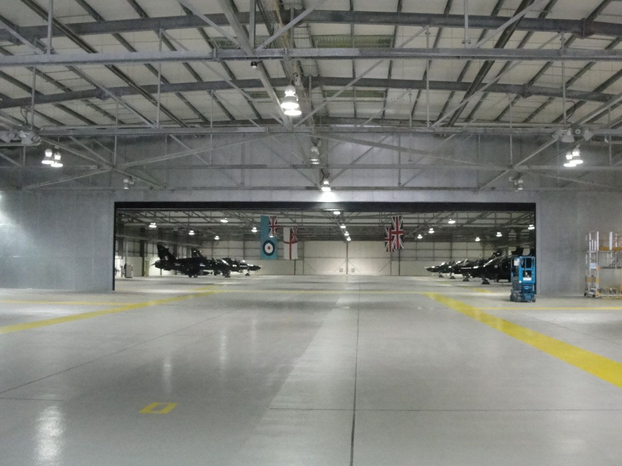 Two fighter jets are parked in a hangar with the door open