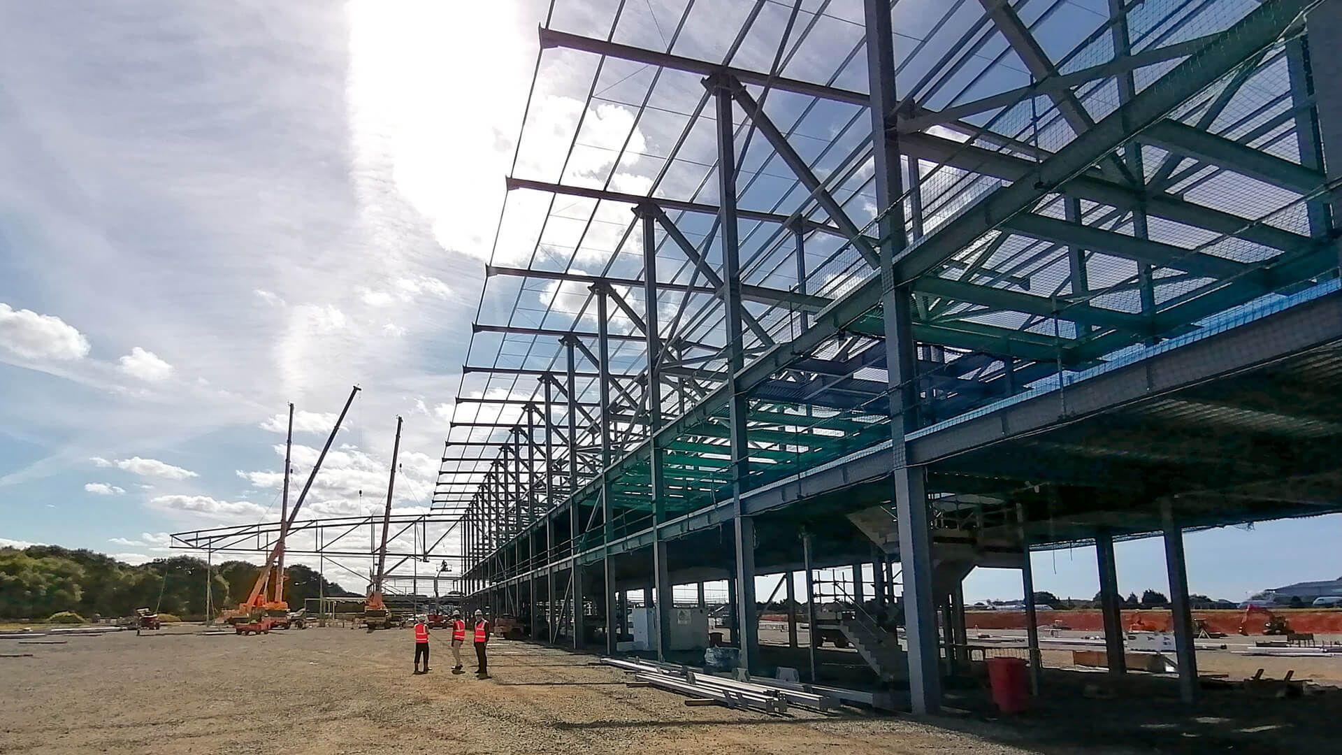 A large metal structure is being built on a dirt field.