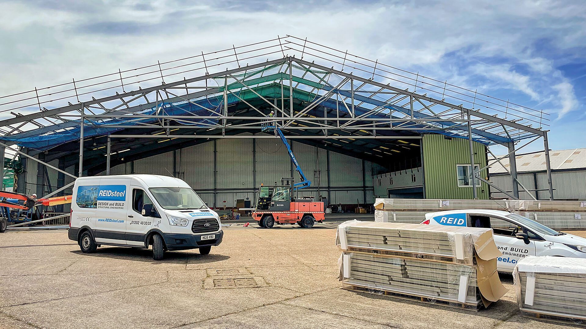 Two vans are parked in front of a building under construction.