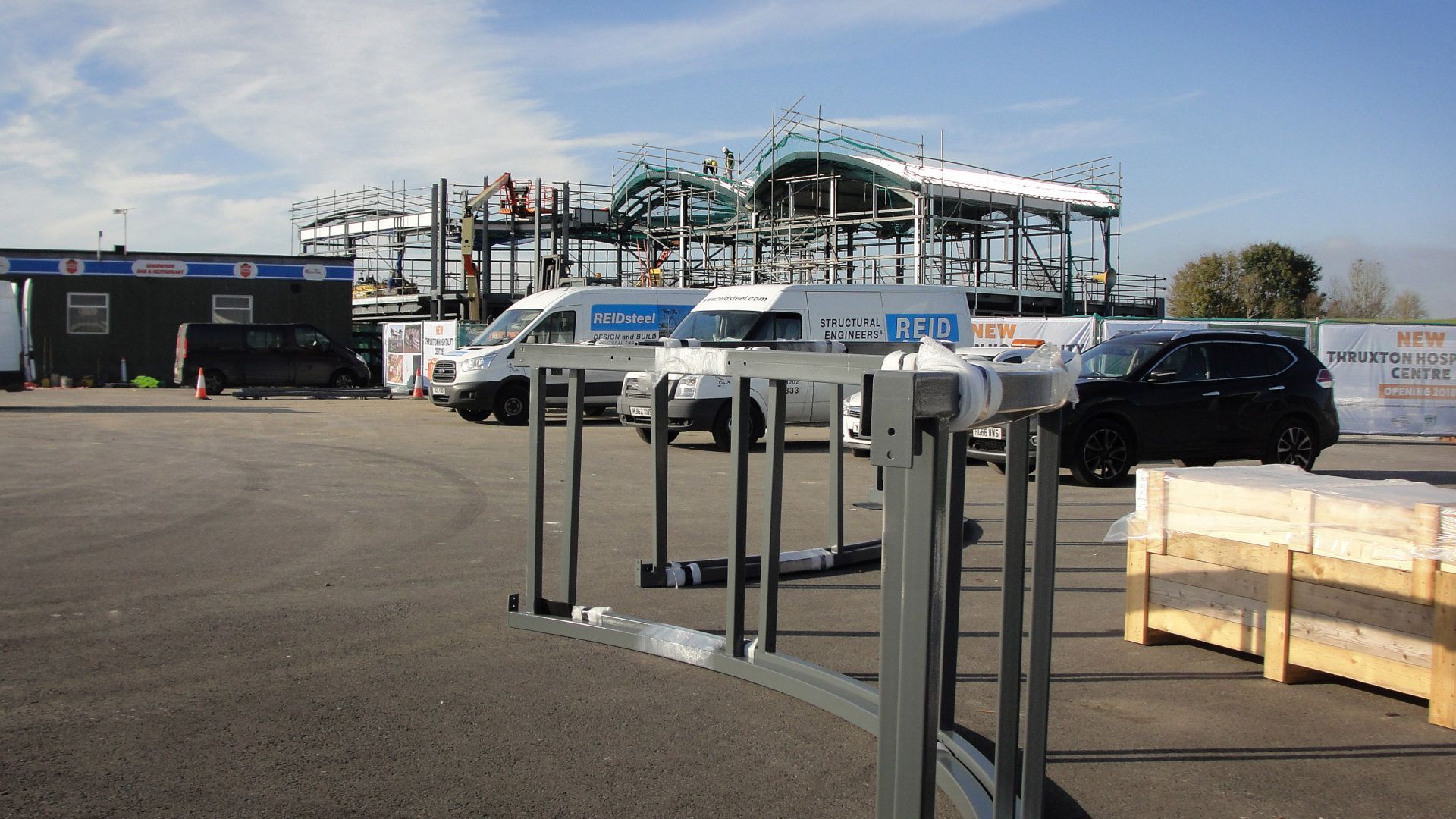 A row of vans are parked in a parking lot in front of a building under construction