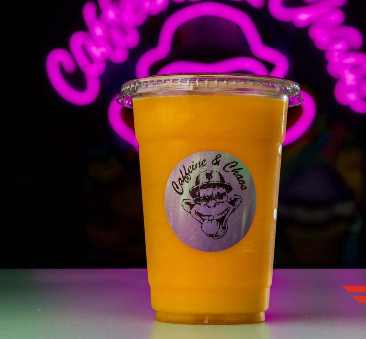Orange-colored drink in a clear cup with a logo sticker, against a neon sign in a dark setting.