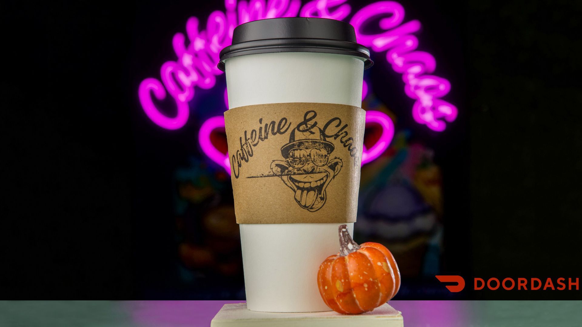 A coffee cup with a sleeve and a jack-o'-lantern against a neon sign that reads 