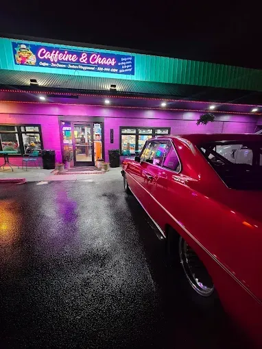 Red classic car parked outside a coffee shop with pink lighting; 
