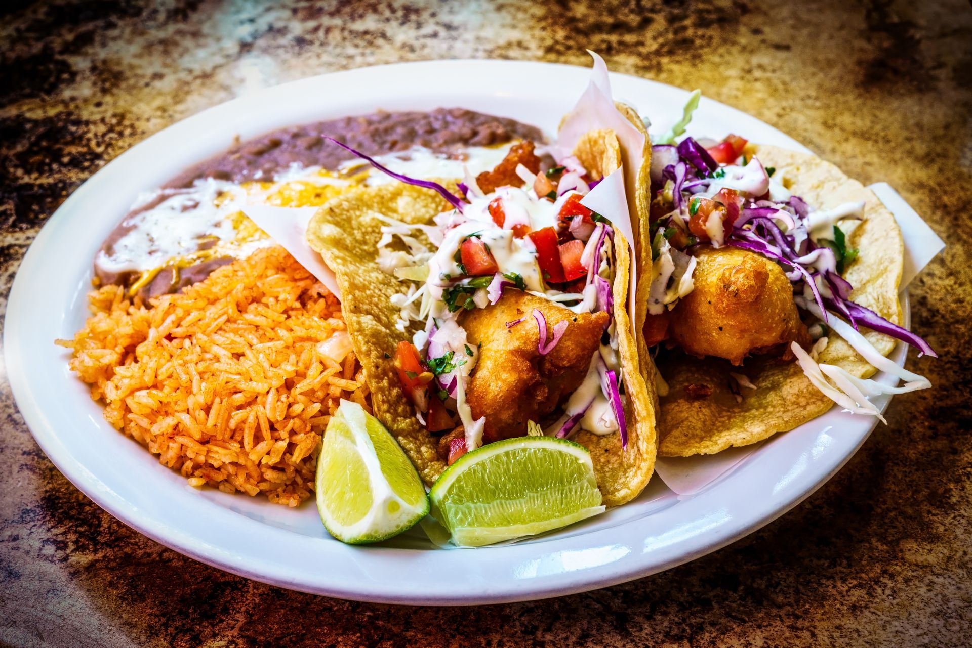 A plate of mexican food with tacos , rice and beans on a table.