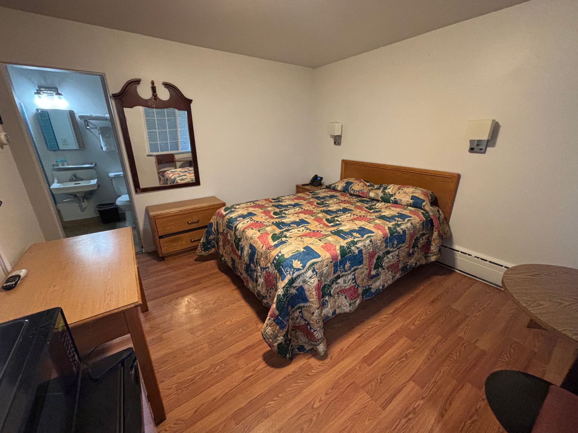 A hotel room with a bed , desk , and mirror.