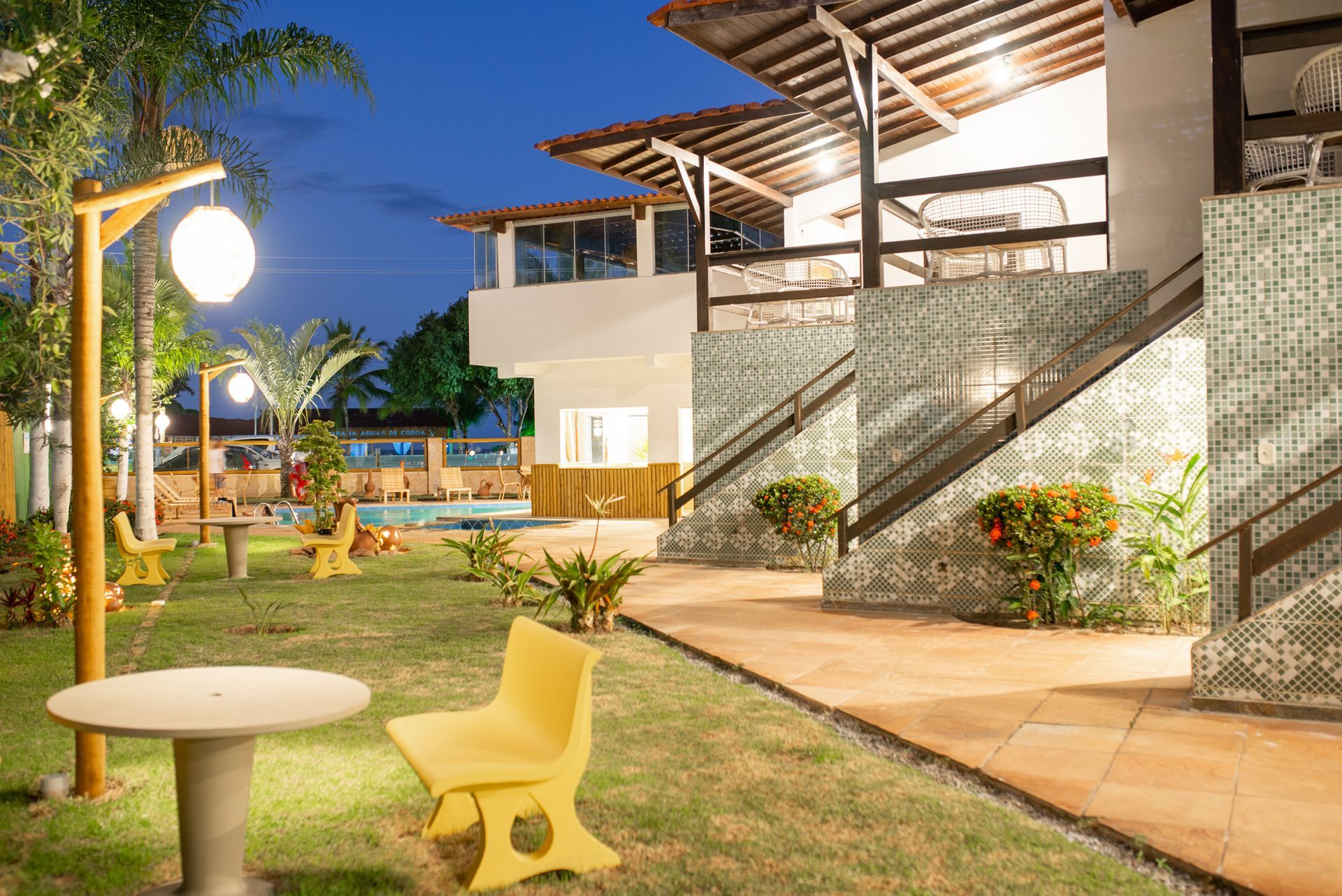 Um gramado com uma mesa e cadeiras em frente a um prédio à noite.