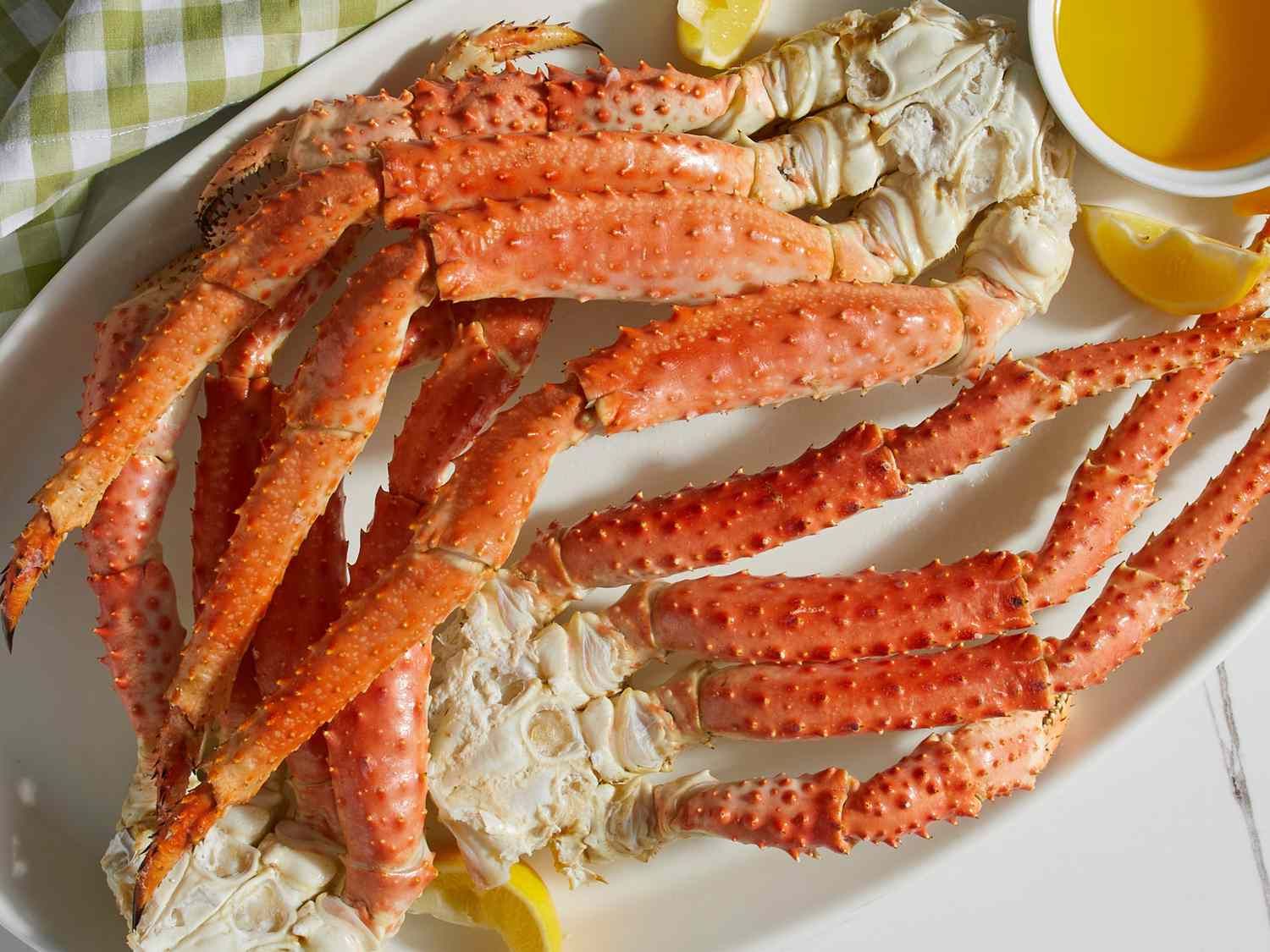 Cooked crab legs on a white platter, with melted butter and lemon wedges.