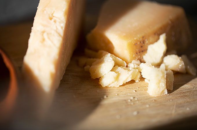 Blocks of Parmesan cheese on a wooden cutting board, with some crumbled pieces.