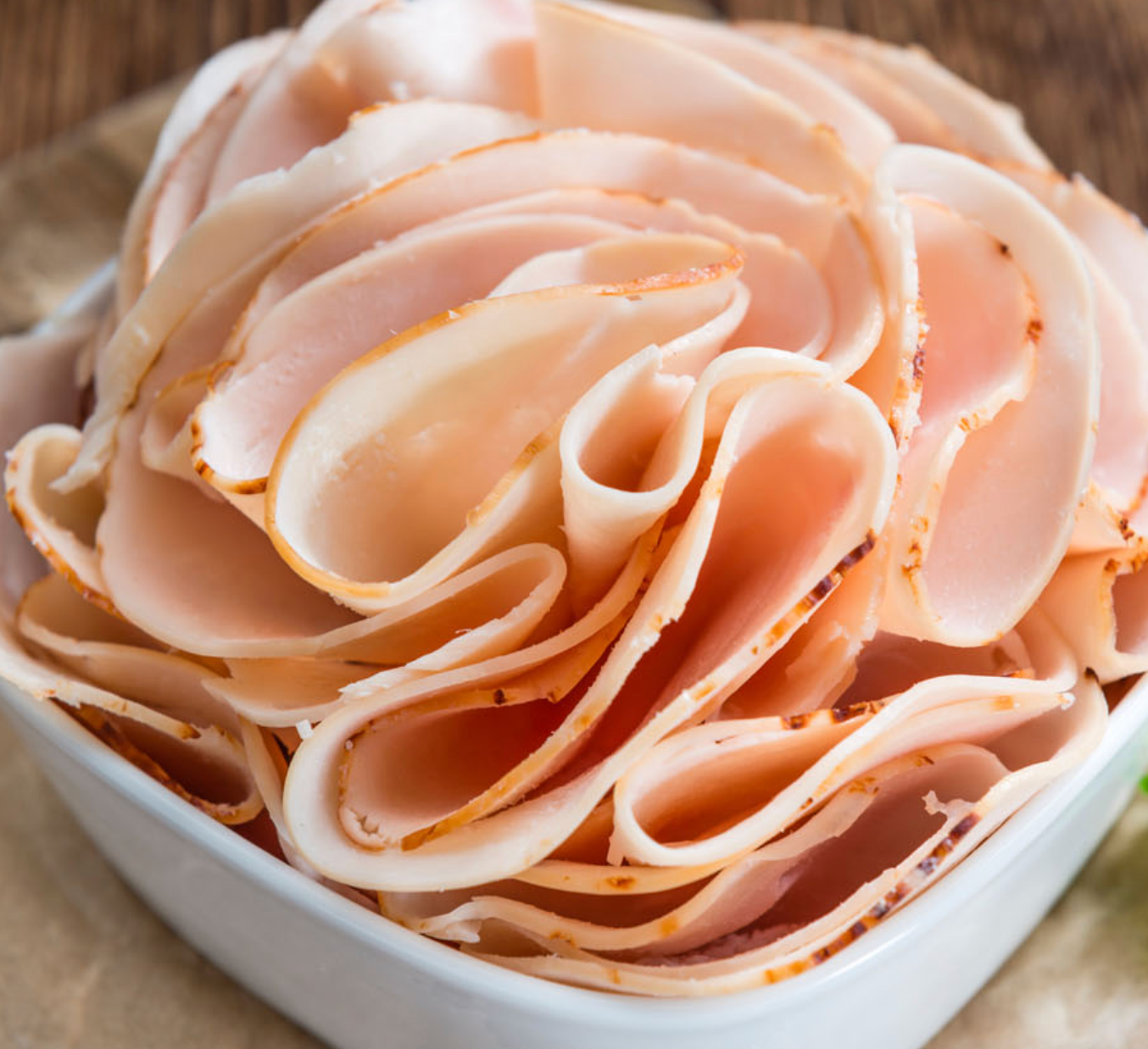 Thinly sliced turkey, light pink and beige, piled in a white square bowl.