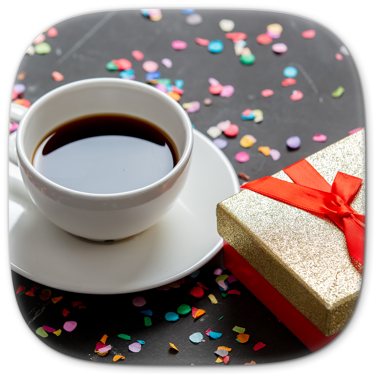 White coffee cup with dark coffee, gift box with red ribbon, confetti on black surface.