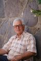 Man with glasses and mustache in patterned shirt sits in front of a stone wall.