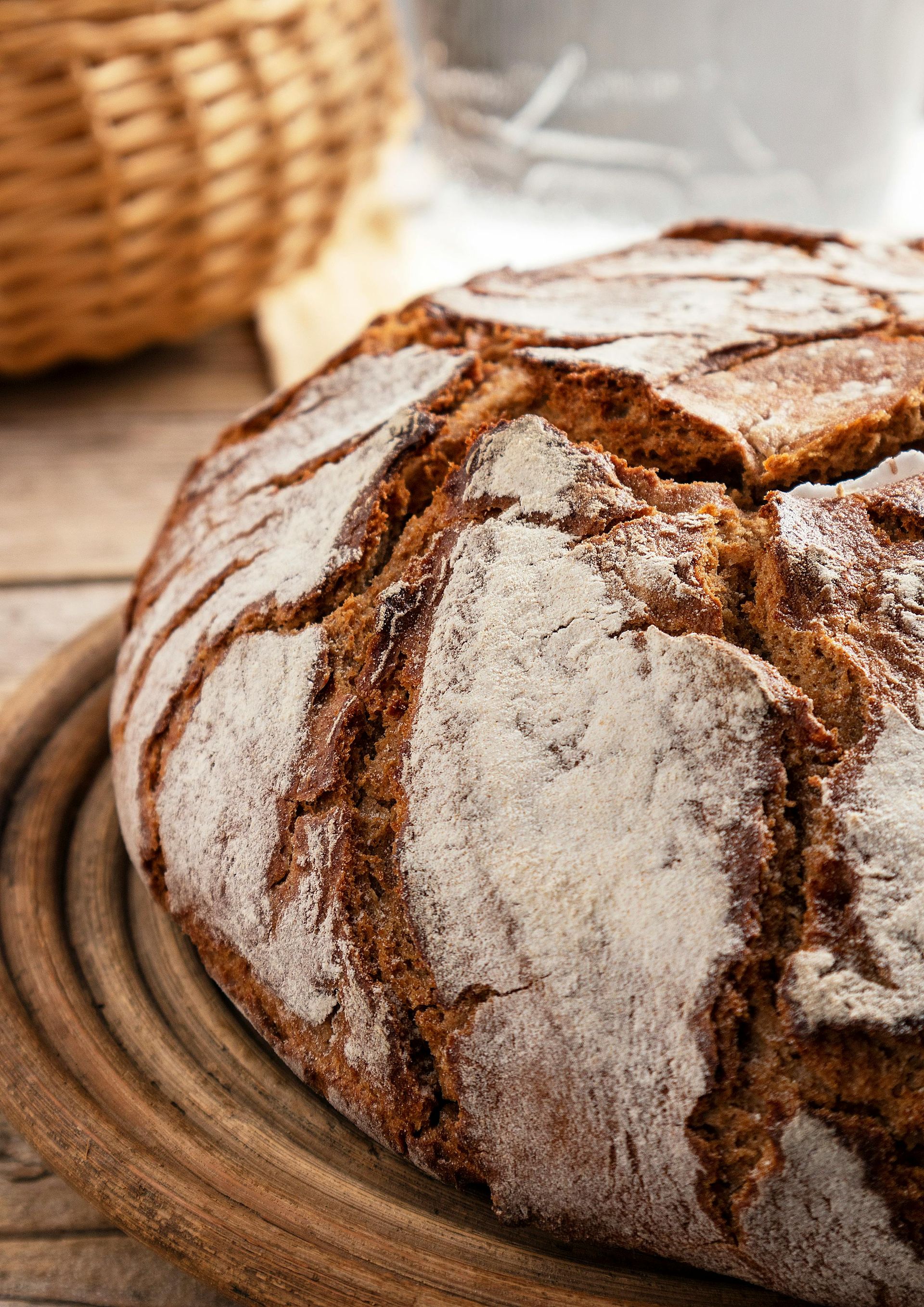 Round loaf of crusty, brown bread dusted with flour on a wooden serving board.