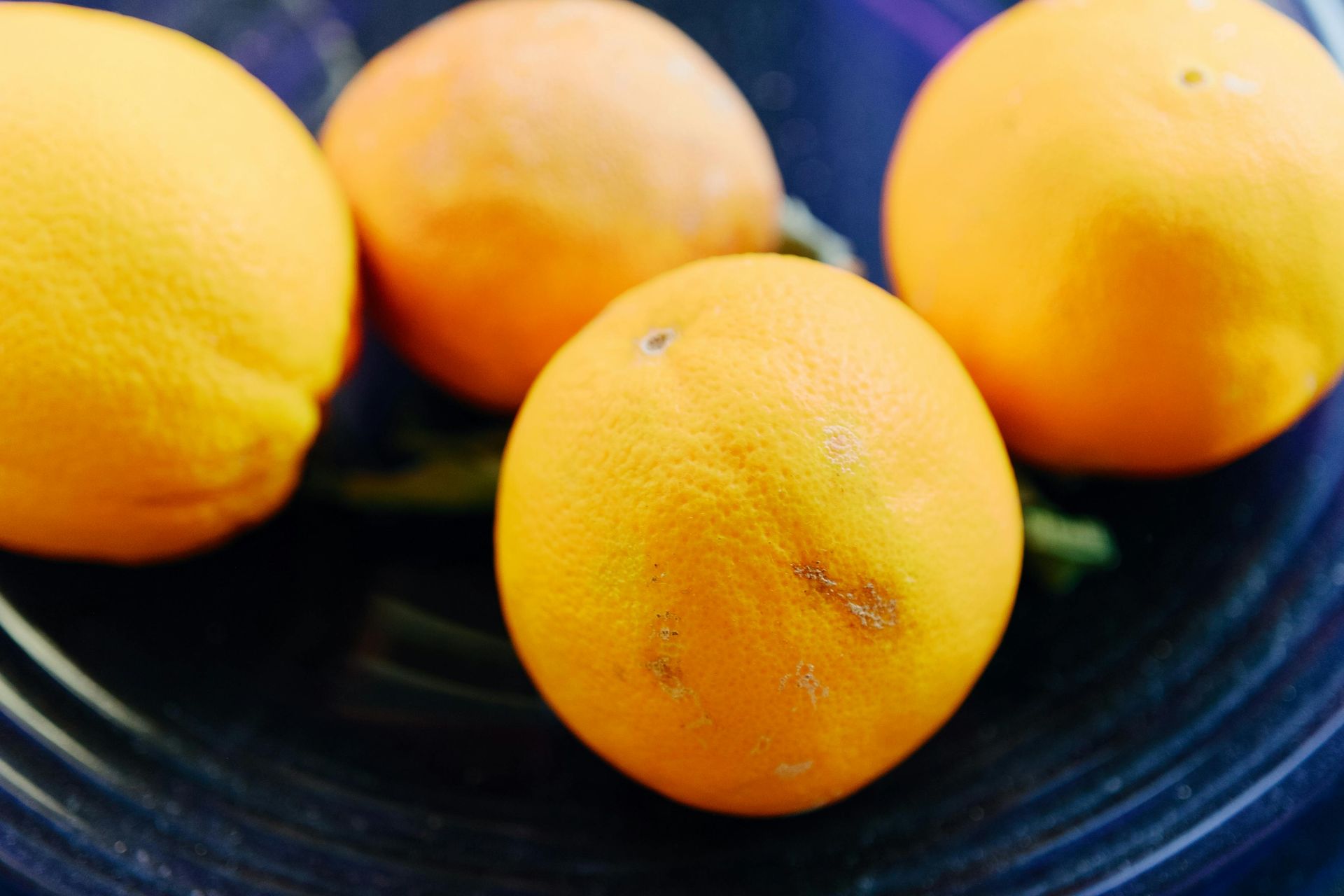 Four oranges in a dark bowl; close up. Bright orange, smooth skins.