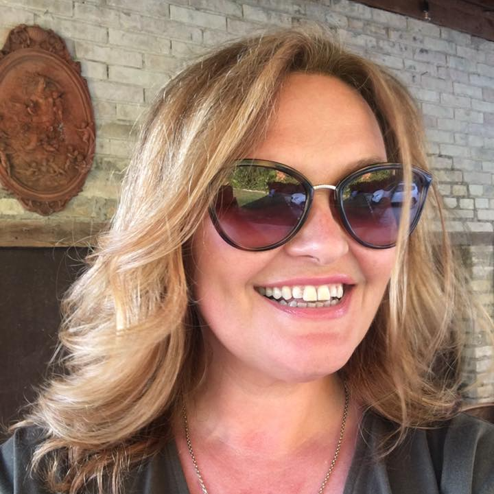 a woman wearing sunglasses is smiling in front of a brick wall .