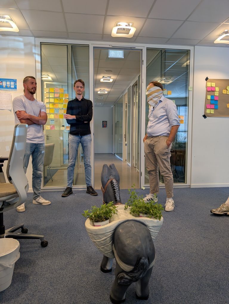 Drie mensen staan in een kantoorgang bij glazen deuren en een display met potplanten.