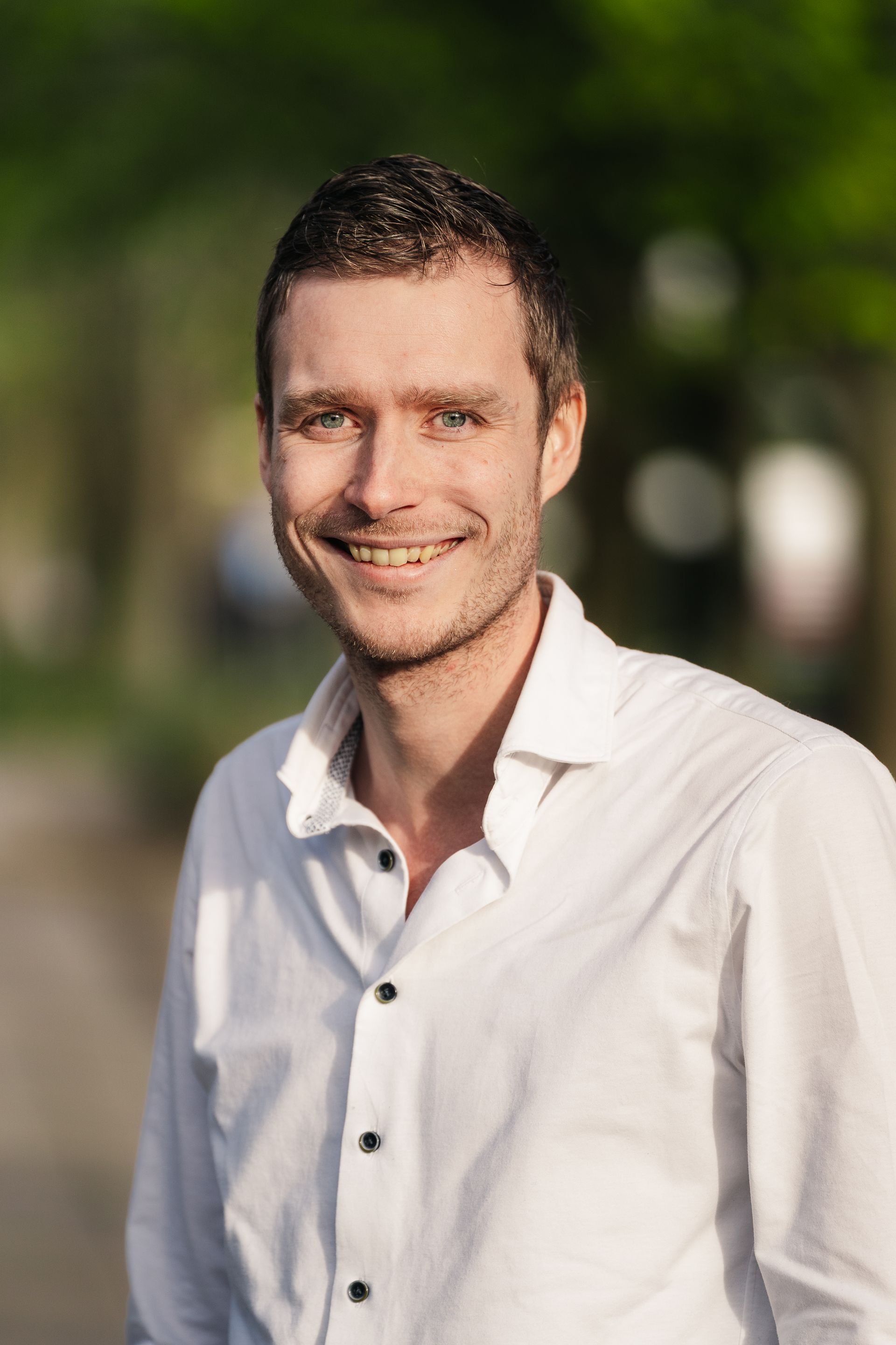 Lachende persoon in een wit shirt buiten met een wazige groene achtergrond.