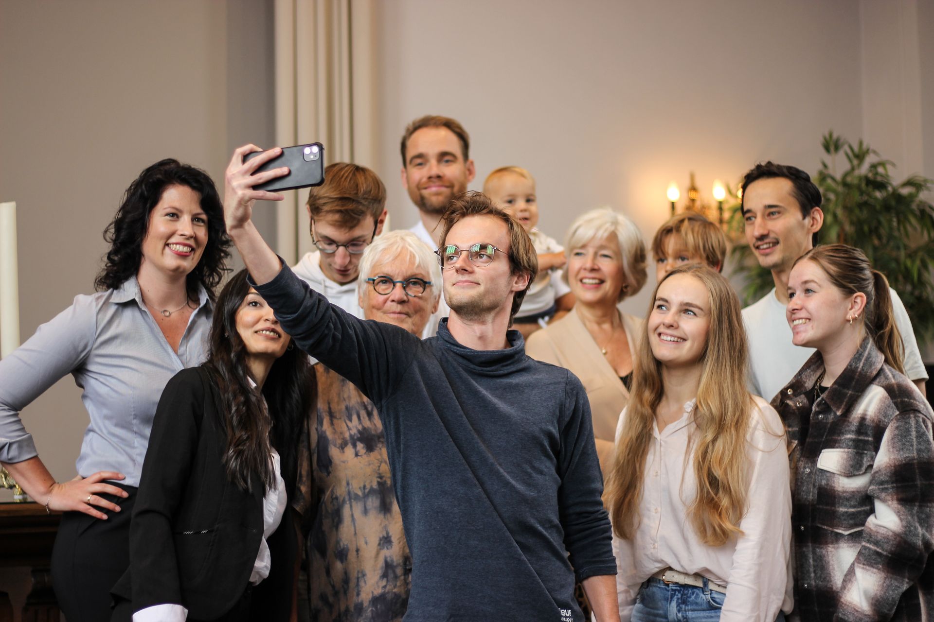 Een groep mensen lacht en maakt een selfie binnen tijdens een bijeenkomst.