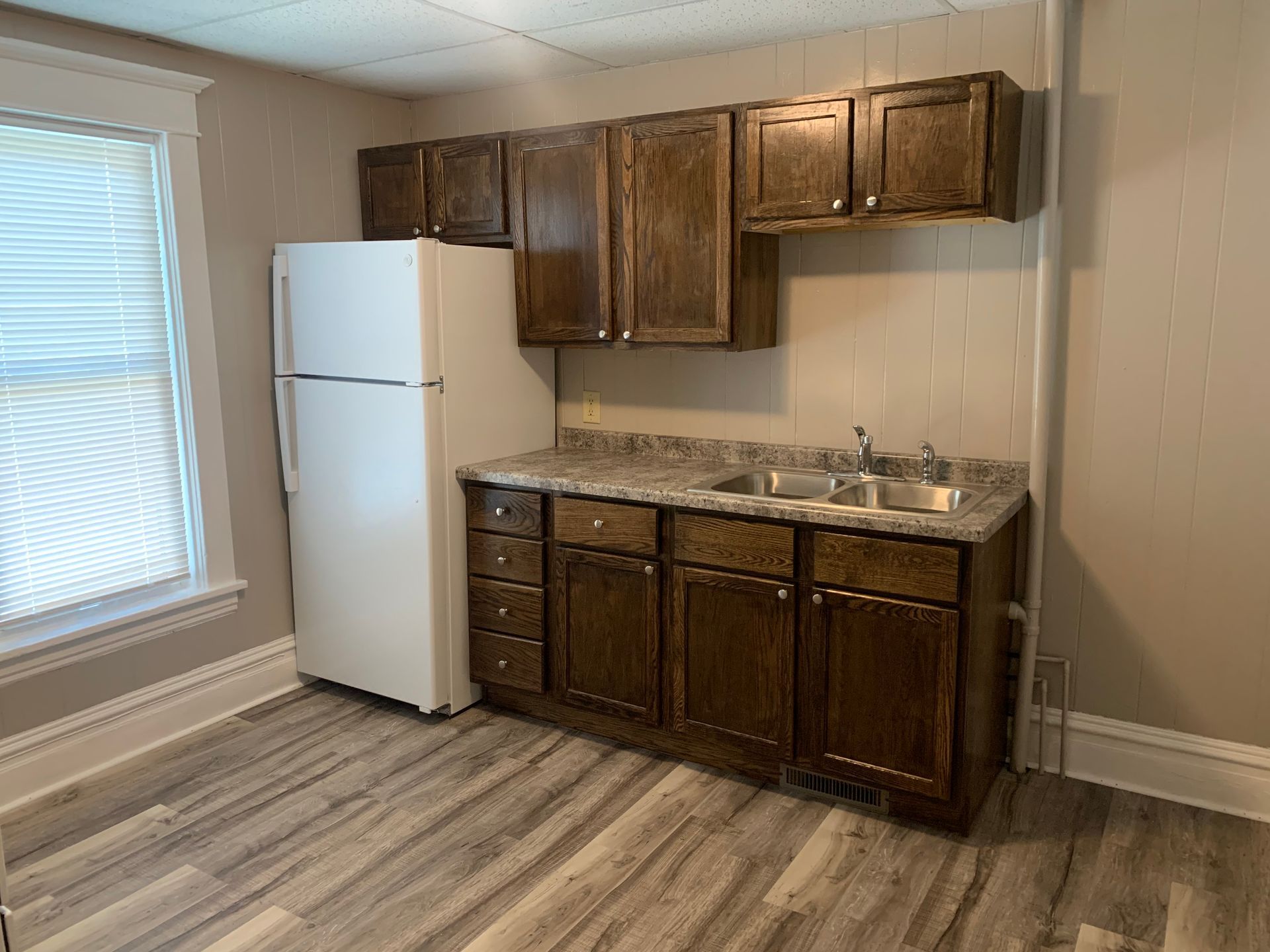 A kitchen with a refrigerator , sink , cabinets and a window.